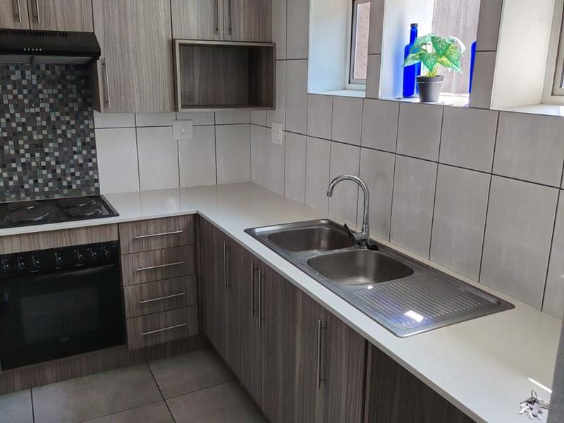 Modern kitchen featuring wood-grain cabinetry, white countertops, mosaic tile splashback, built-in oven, hob, and a stainless steel double sink with mixer tap.
