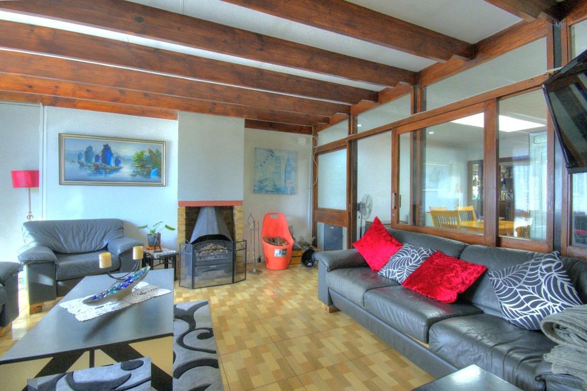 Living room featuring exposed timber ceiling beams, a brick-surround fireplace, and a unique timber-framed glass partition wall looking into the adjacent space.