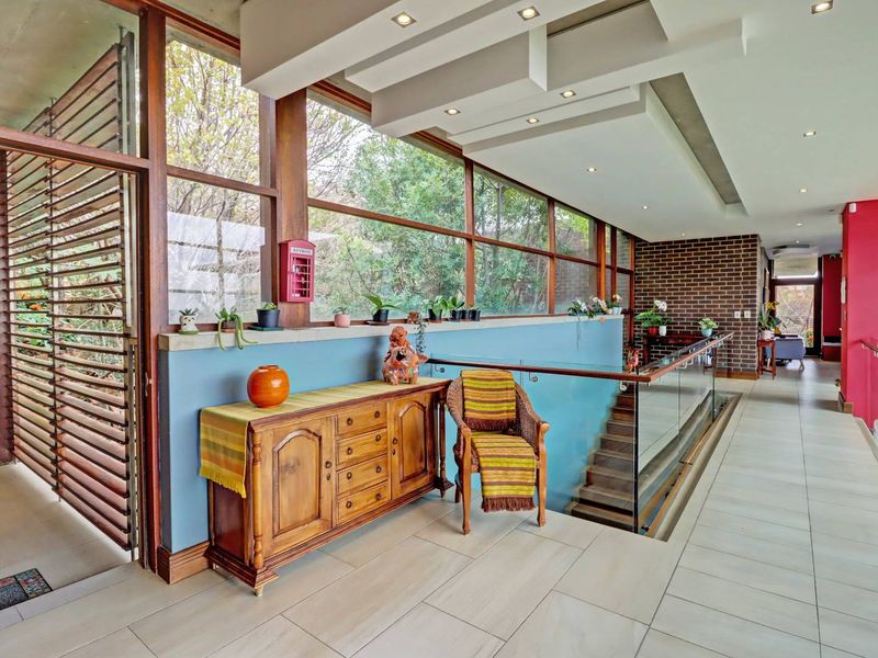 Spacious hallway featuring modern recessed ceiling lighting, a glass balustrade overlooking the staircase, and expansive windows with views of the surrounding greenery.