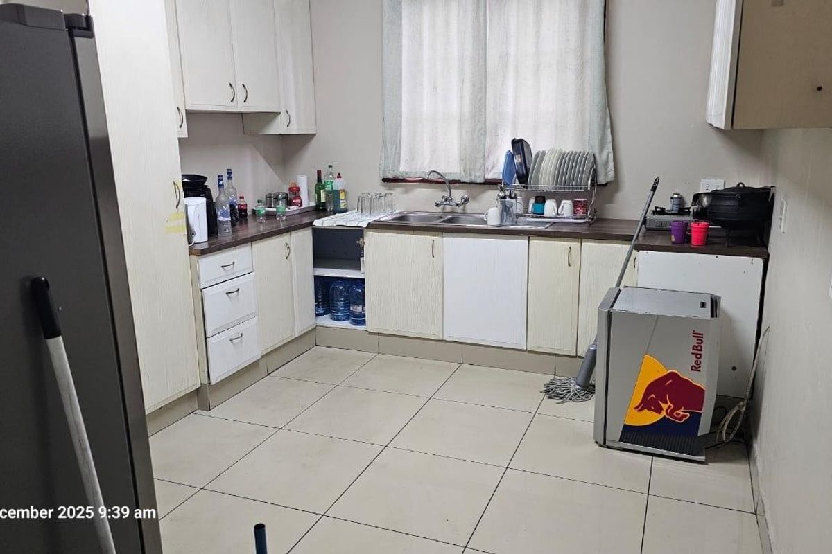 A functional kitchen featuring laminate cabinetry, a double sink, and tiled flooring, offering a practical layout with potential for cosmetic updates.