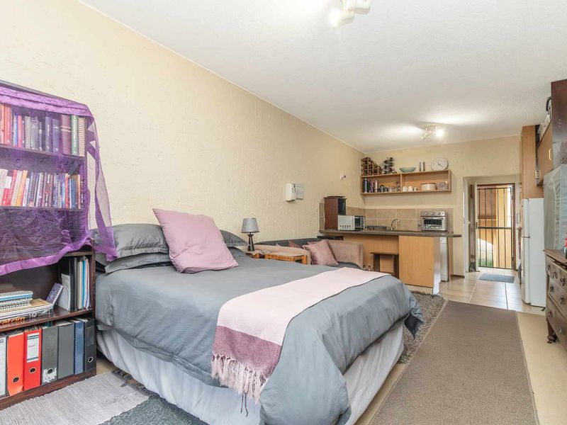 Open-plan studio apartment featuring a compact kitchenette with tiled backsplash and built-in shelving, providing a functional living and sleeping space.