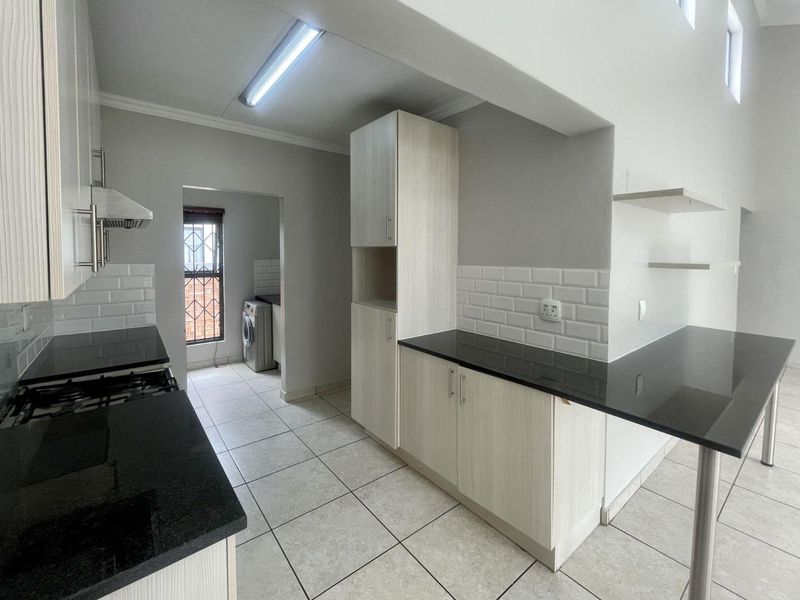 Modern kitchen featuring light wood cabinetry, granite countertops, subway tile backsplash, and a breakfast bar, with an adjoining scullery area.