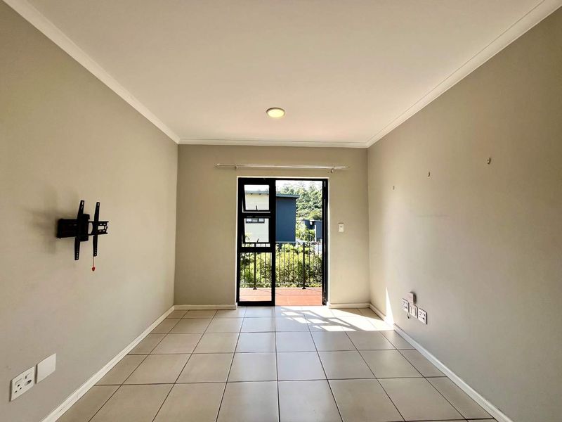 An empty living room featuring neutral tiled flooring and a glass door leading to an outdoor balcony area.