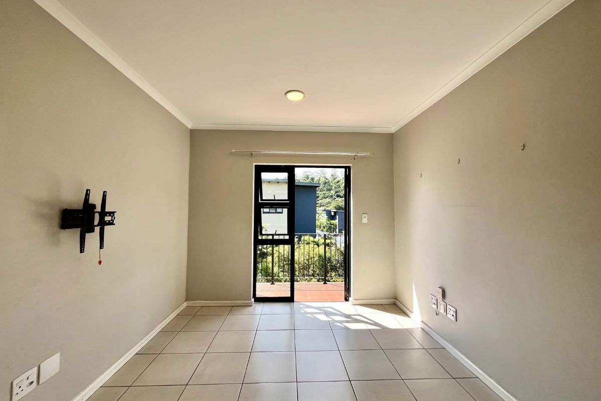 An empty living room featuring neutral tiled flooring and a glass door leading to an outdoor balcony area.