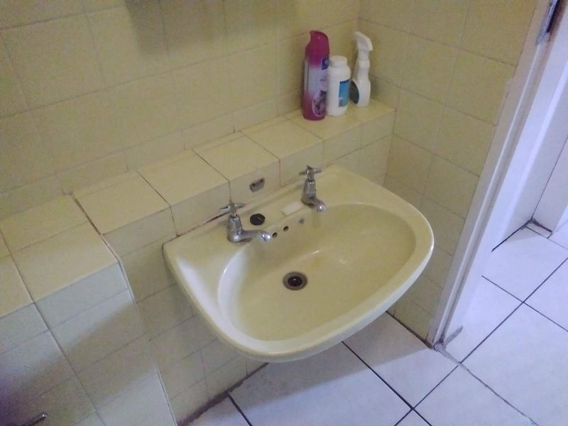 A dated bathroom featuring a wall-mounted basin with tiled splashback and ceramic floor tiles, requiring modernization to improve aesthetic appeal.