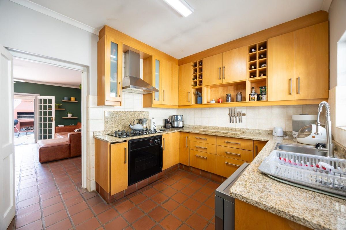 Functional kitchen featuring warm-toned wooden cabinetry, granite countertops, gas hob, built-in oven, and tiled flooring with direct access to an adjacent living area.