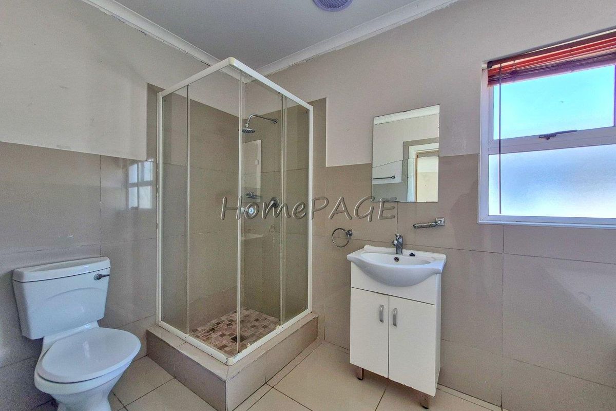 A functional bathroom featuring a glass-enclosed shower, a pedestal vanity with a basin, and a standard toilet, finished with neutral wall and floor tiling.