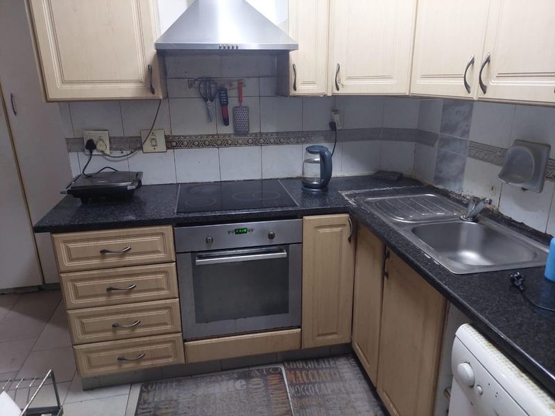 A compact kitchen featuring dated cabinetry, a built-in oven with electric hob, stainless steel extractor fan, and a double bowl sink with granite countertops.