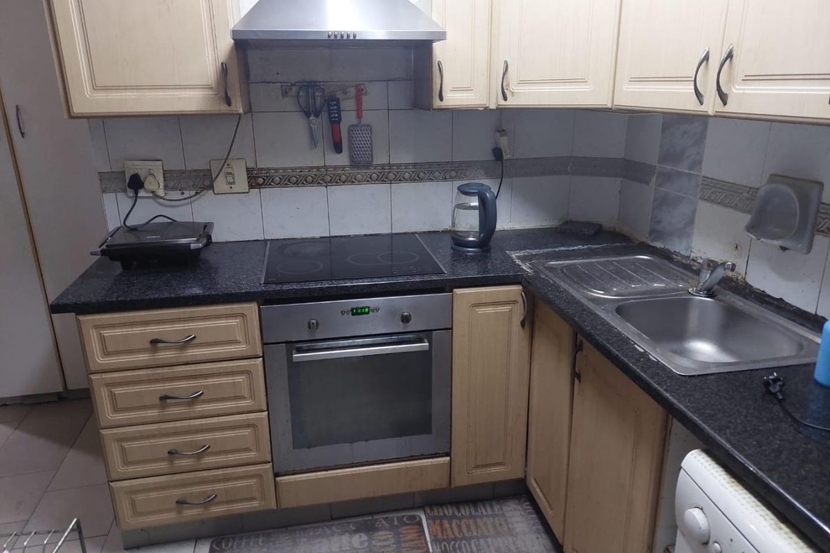 A compact kitchen featuring dated cabinetry, a built-in oven with electric hob, stainless steel extractor fan, and a double bowl sink with granite countertops.