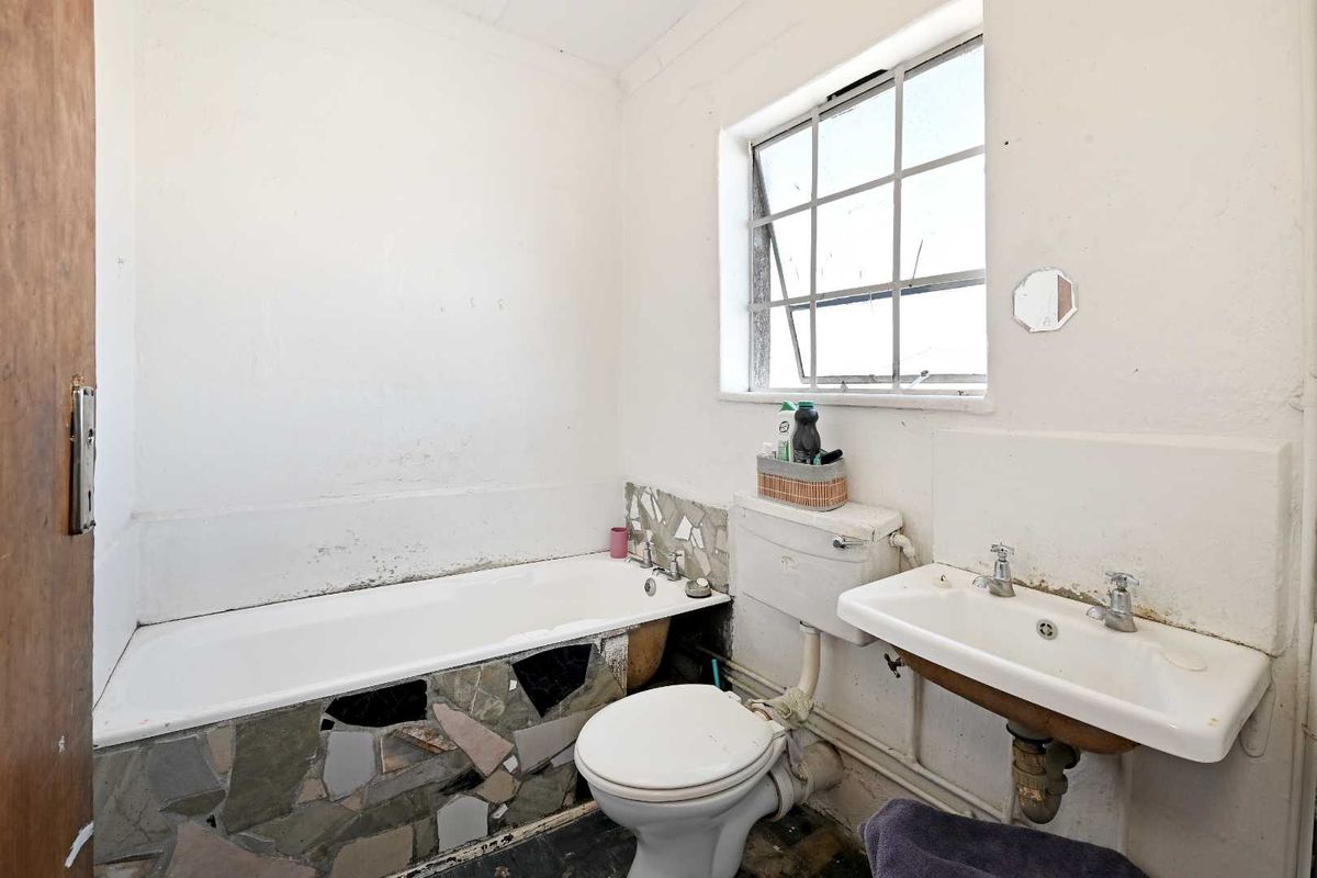 A dated bathroom featuring a bathtub with stone cladding, a wall-mounted basin, and a toilet, requiring significant renovation and cosmetic updates.
