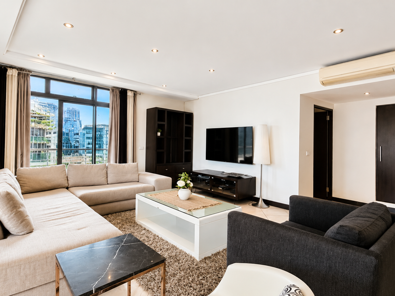 A bright and spacious living room featuring tiled flooring, recessed downlighting, a split-system air conditioner, and large windows with city views.