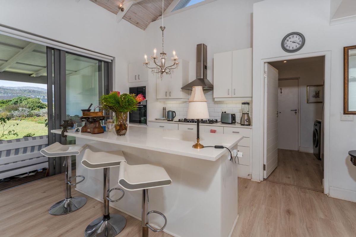 Modern kitchen featuring a central island with breakfast bar, white cabinetry, stainless steel extractor fan, and vaulted ceilings with exposed beams.