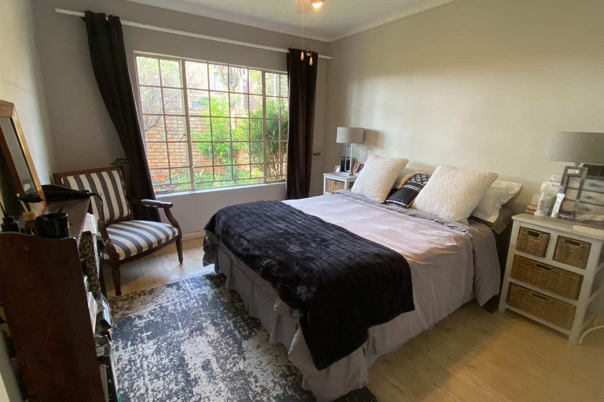 A well-lit bedroom featuring laminate flooring, a ceiling fan, and a large window overlooking the garden area.