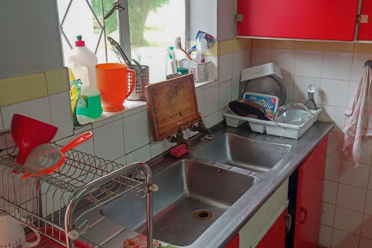 A dated kitchen sink area featuring a stainless steel double basin, red cabinetry, and tiled splashbacks under a window.