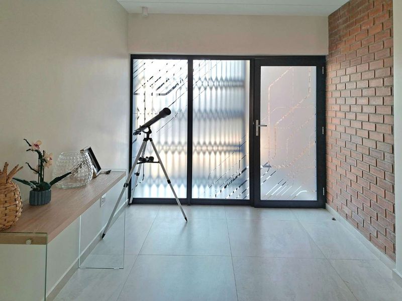 A bright entrance area featuring modern tiled flooring, an exposed brick feature wall, and a contemporary frosted glass door providing natural light.