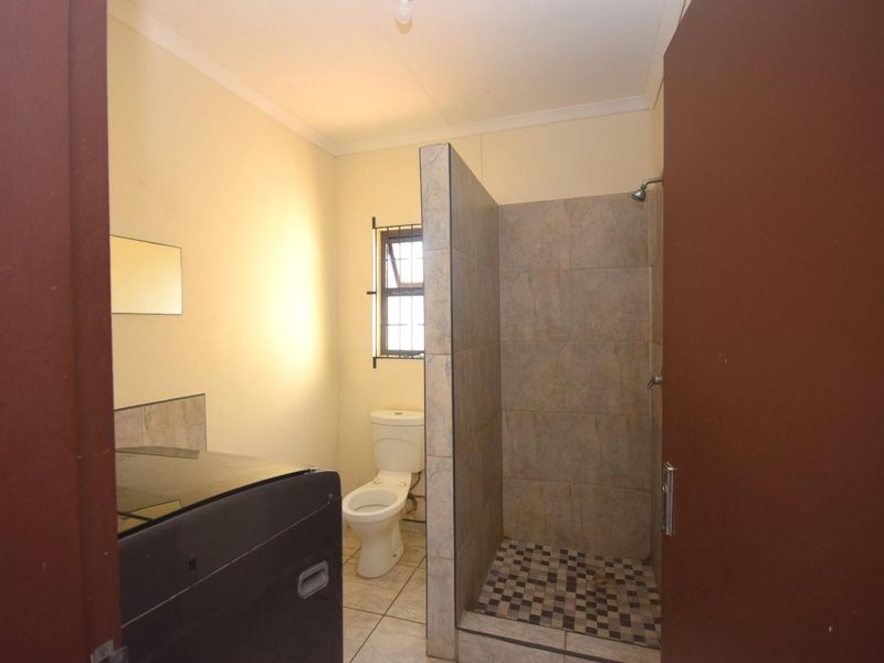 A functional bathroom featuring a walk-in shower with tiled enclosure, a standard toilet, and tiled flooring.