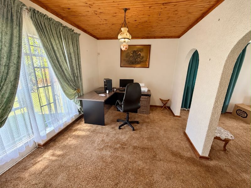 A home office space featuring a timber-clad ceiling, textured walls, and an arched entryway, providing a functional workspace with natural light.