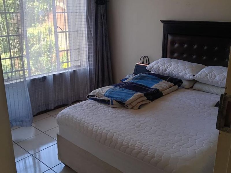 A functional bedroom featuring tiled flooring and a large window with security bars, providing natural light.