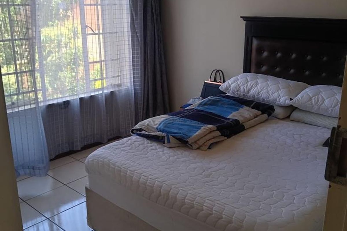 A functional bedroom featuring tiled flooring and a large window with security bars, providing natural light.