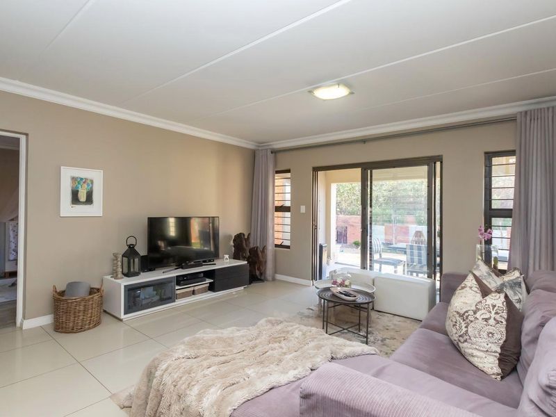 A well-maintained living room featuring neutral tiled flooring, coved ceilings, and large sliding glass doors that provide access to the outdoor patio area.