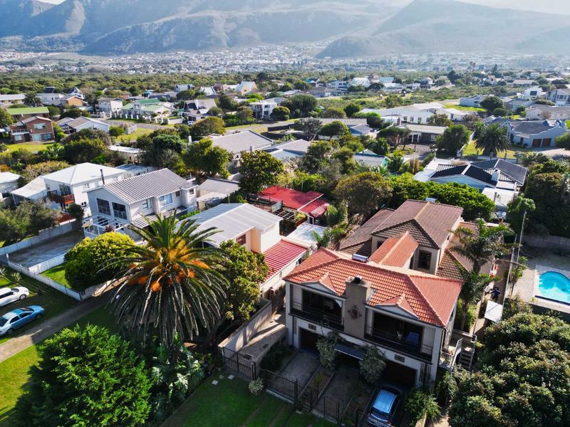 Aerial view of the property showcasing the multi-level house with terracotta roof tiles, balconies, a paved driveway, and a swimming pool in a residential setting.