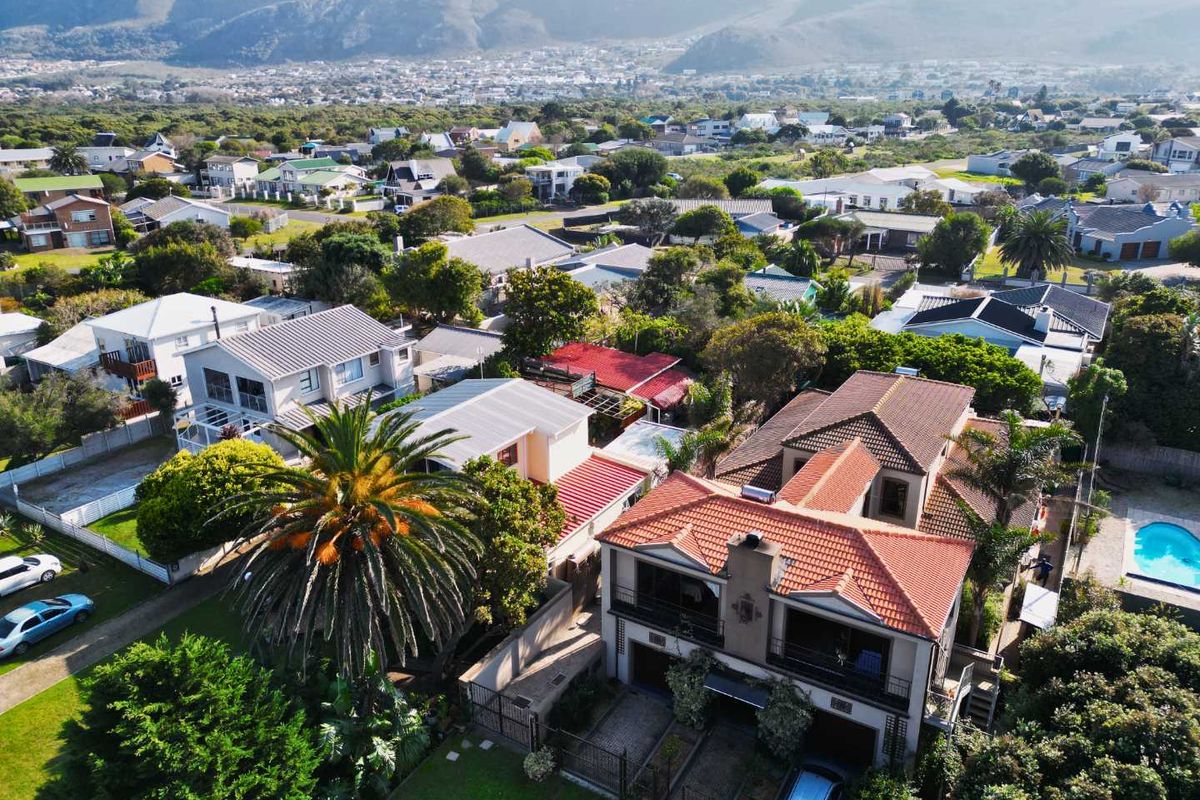 Aerial view of the property showcasing the multi-level house with terracotta roof tiles, balconies, a paved driveway, and a swimming pool in a residential setting.