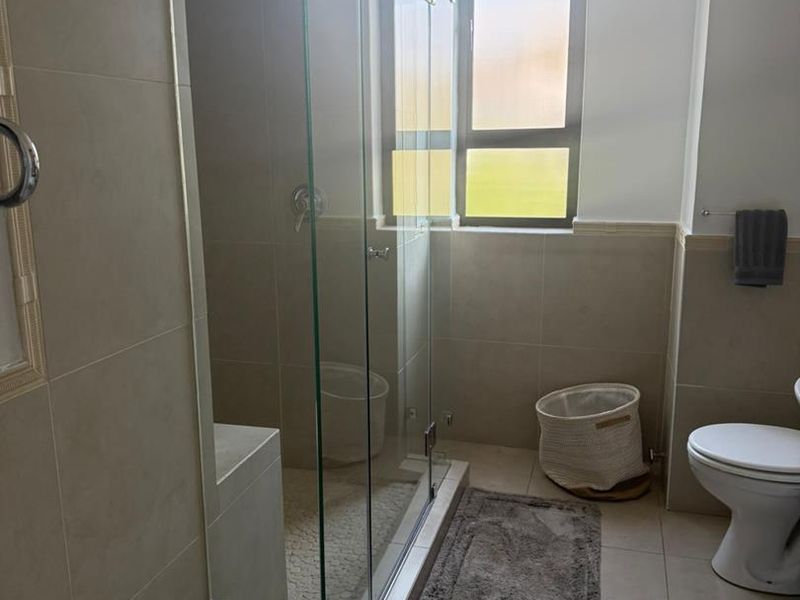 A modern bathroom featuring a spacious glass-enclosed shower with a built-in bench, pebble tile flooring, and neutral ceramic wall tiles.