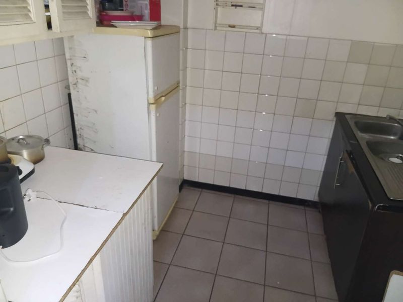 A compact kitchen featuring tiled splashbacks, a double bowl sink, and dated cabinetry, offering potential for a modern renovation.