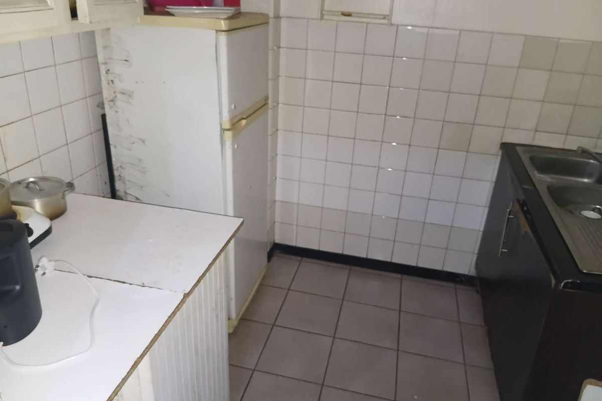 A compact kitchen featuring tiled splashbacks, a double bowl sink, and dated cabinetry, offering potential for a modern renovation.