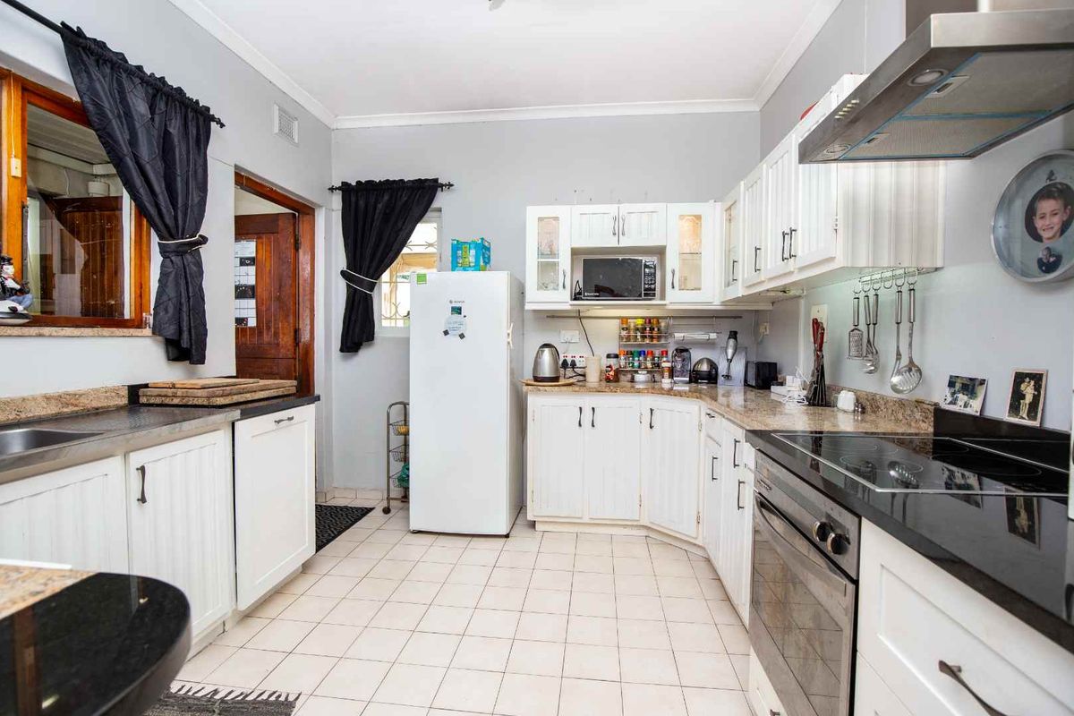 A functional kitchen featuring white cabinetry, granite countertops, built-in oven, and electric hob with an extractor fan.