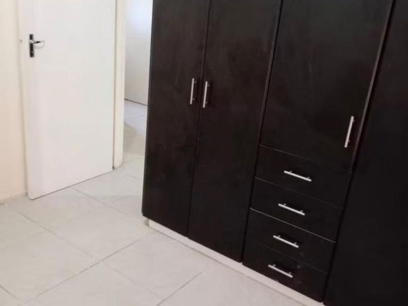 A clean, empty bedroom featuring dark wood built-in cupboards and neutral tiled flooring, offering a blank canvas for personalization.