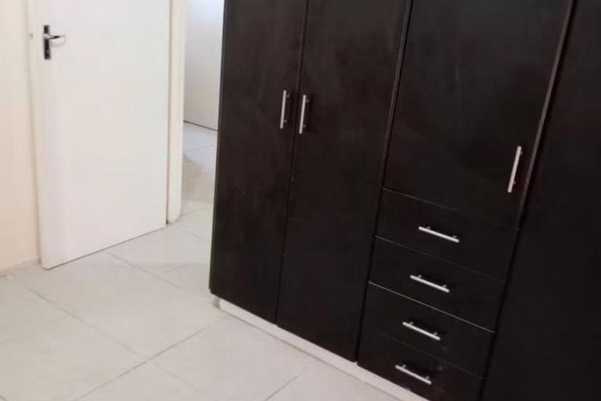 A clean, empty bedroom featuring dark wood built-in cupboards and neutral tiled flooring, offering a blank canvas for personalization.
