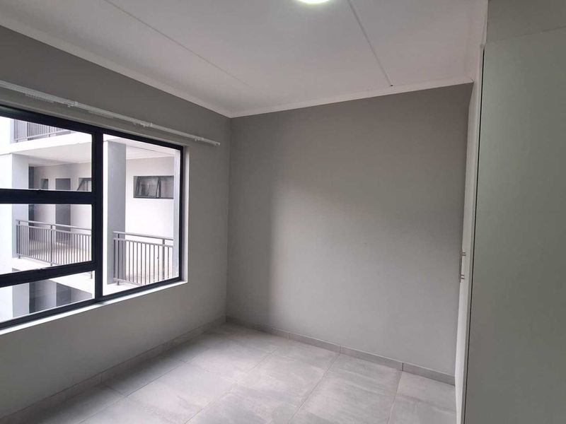 A clean, empty bedroom featuring neutral grey walls, tiled flooring, and a built-in wardrobe, offering a blank canvas for personalization.
