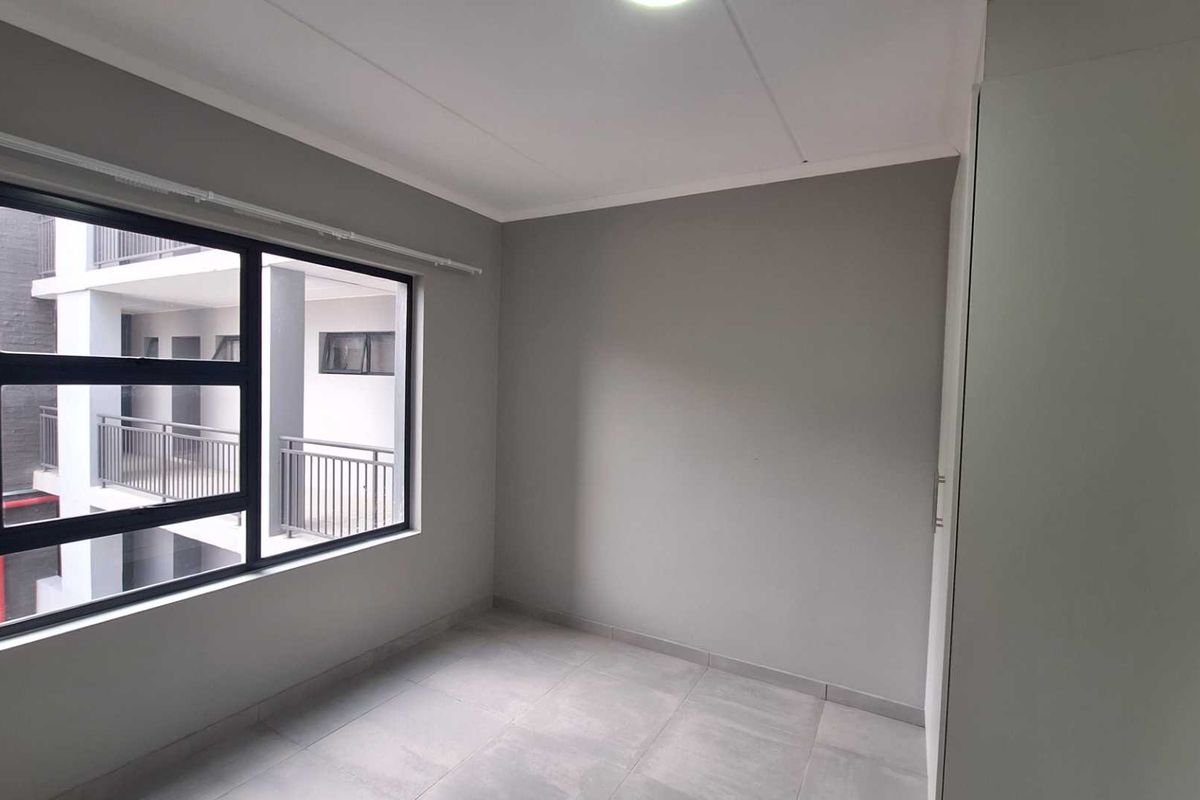 A clean, empty bedroom featuring neutral grey walls, tiled flooring, and a built-in wardrobe, offering a blank canvas for personalization.