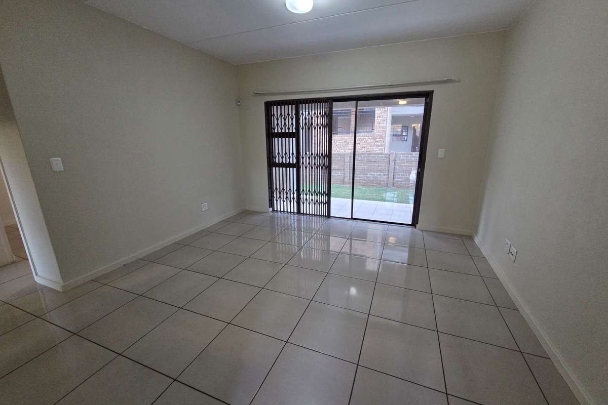 An empty living room featuring neutral tiled flooring and a sliding glass door with a security gate leading to an outdoor area.
