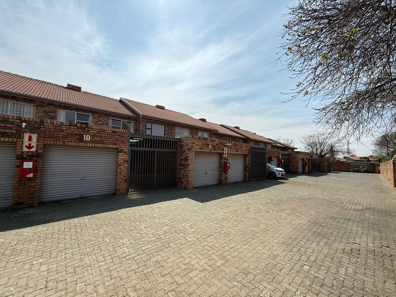 A row of face brick cluster units featuring individual roll-up garage doors and a paved driveway area.