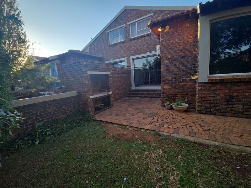 Rear exterior view of the townhouse featuring a brick facade, paved patio area, and a built-in brick braai.