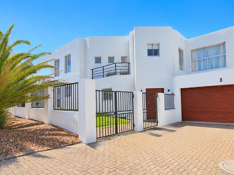 Front elevation of a modern white house featuring a paved driveway, integrated garage, and secure metal fencing.