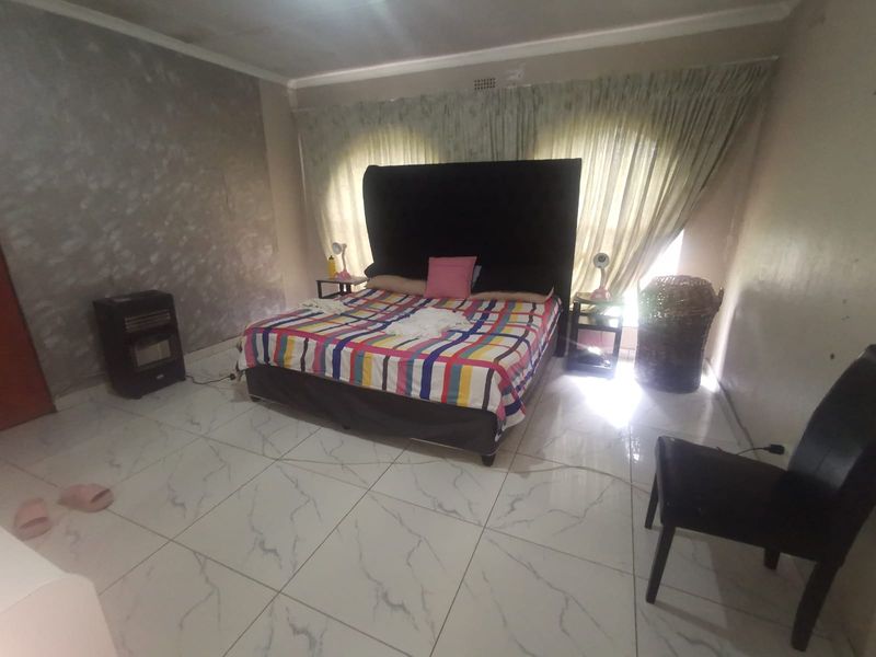 A bedroom featuring large format marble-look floor tiles, a textured feature wall, and window curtains.
