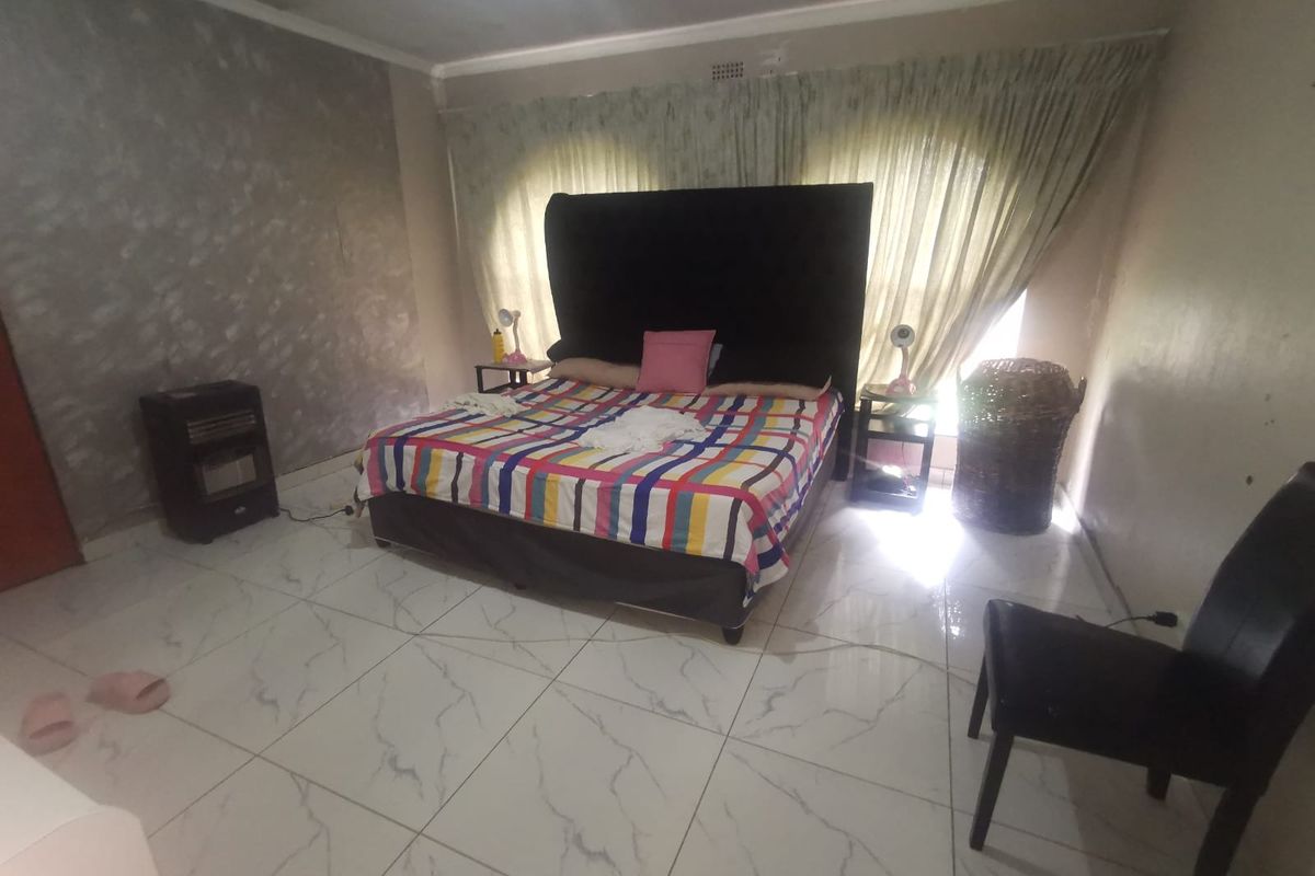 A bedroom featuring large format marble-look floor tiles, a textured feature wall, and window curtains.