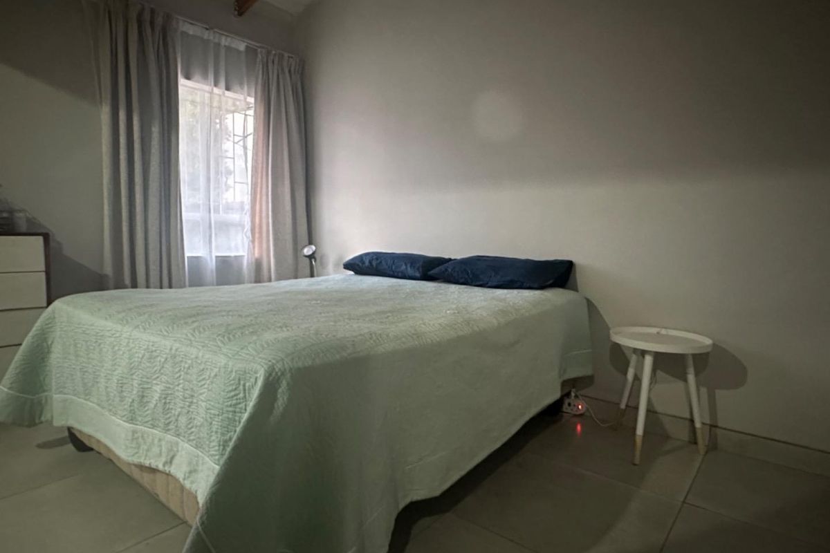 A functional bedroom featuring tiled flooring and a window with curtain tracks.