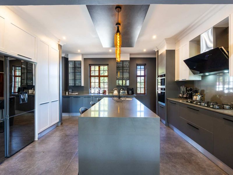 Modern, high-end kitchen featuring a large central island, sleek dark cabinetry, stone countertops, integrated appliances, and sophisticated pendant lighting.