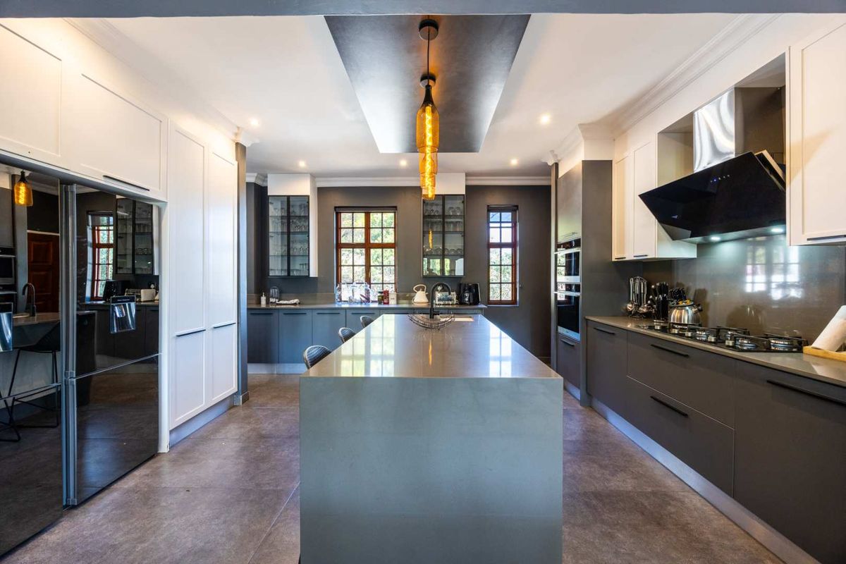 Modern, high-end kitchen featuring a large central island, sleek dark cabinetry, stone countertops, integrated appliances, and sophisticated pendant lighting.
