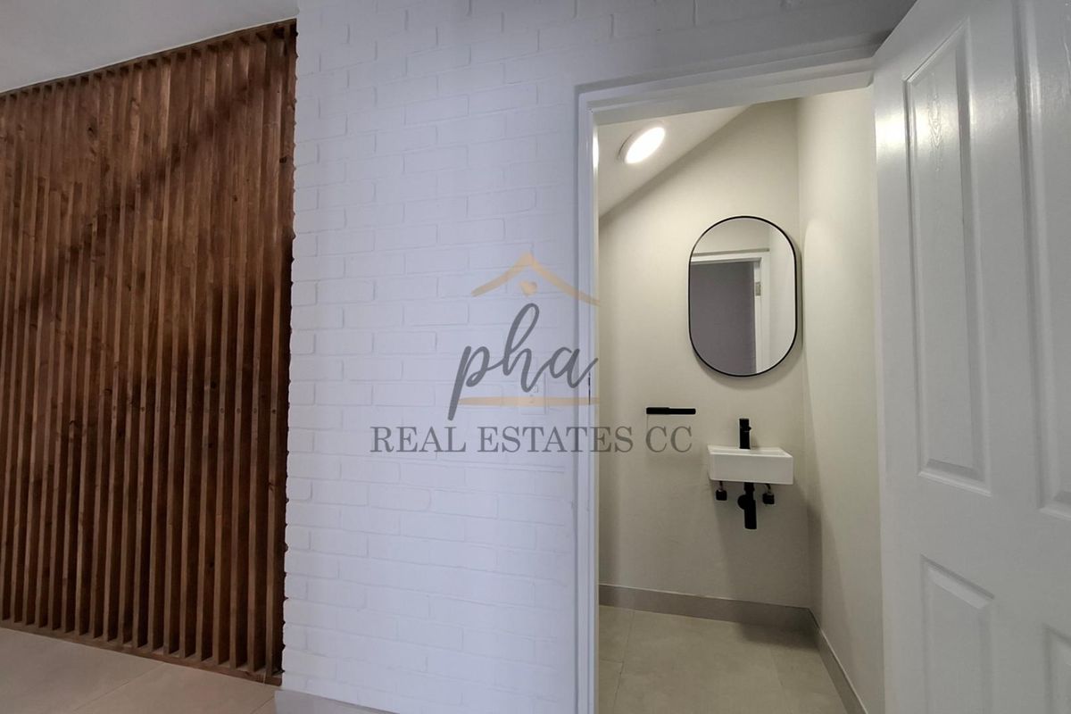 A modern guest bathroom featuring a wall-mounted basin, black fixtures, and a stylish timber slat feature wall in the adjacent hallway.