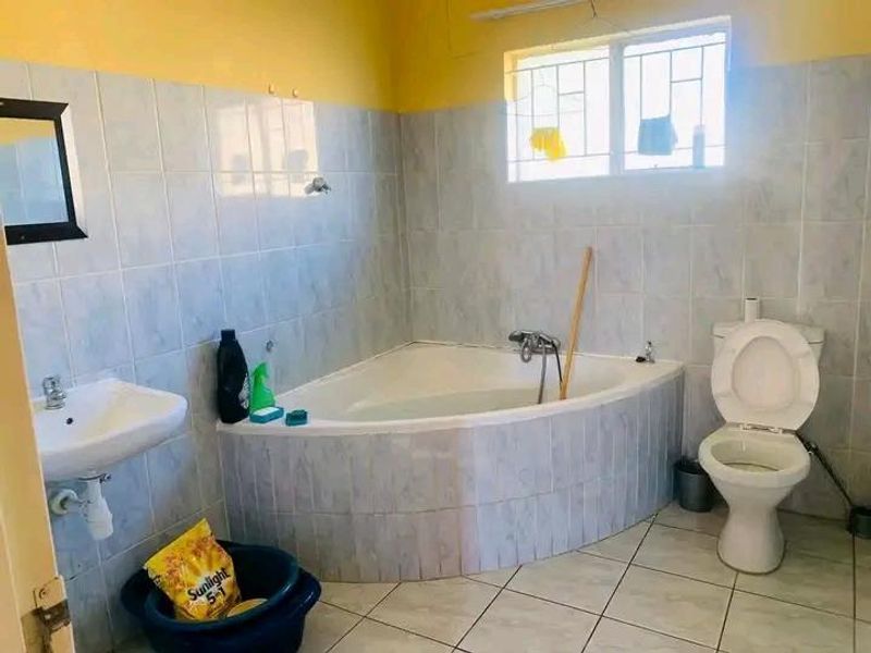 A functional bathroom featuring a corner bathtub, pedestal basin, and toilet with tiled walls and flooring.