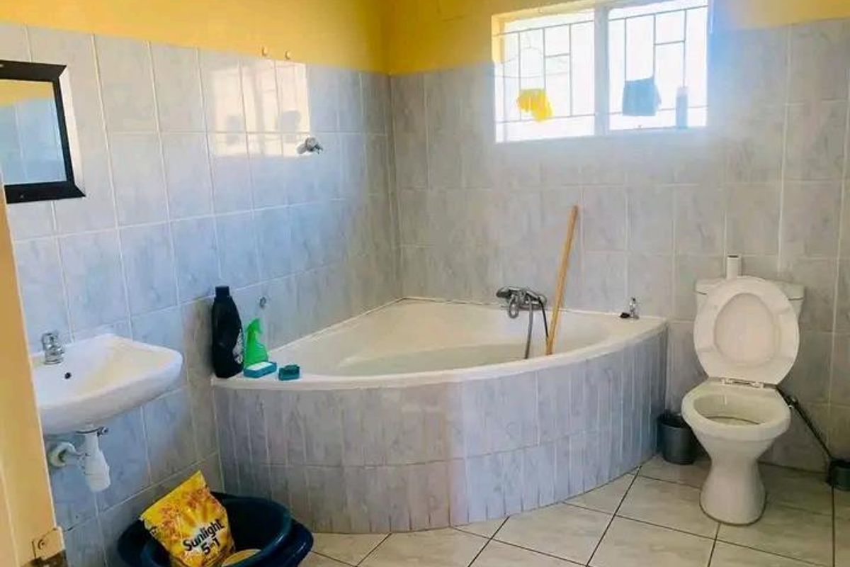 A functional bathroom featuring a corner bathtub, pedestal basin, and toilet with tiled walls and flooring.