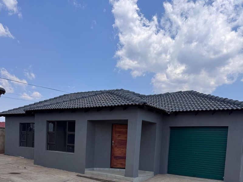 Modern townhouse exterior featuring a dark grey facade, tiled roof, timber entrance door, and a secure garage with a green roller door.