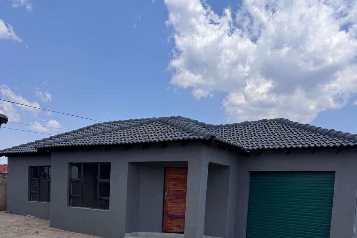 Modern townhouse exterior featuring a dark grey facade, tiled roof, timber entrance door, and a secure garage with a green roller door.