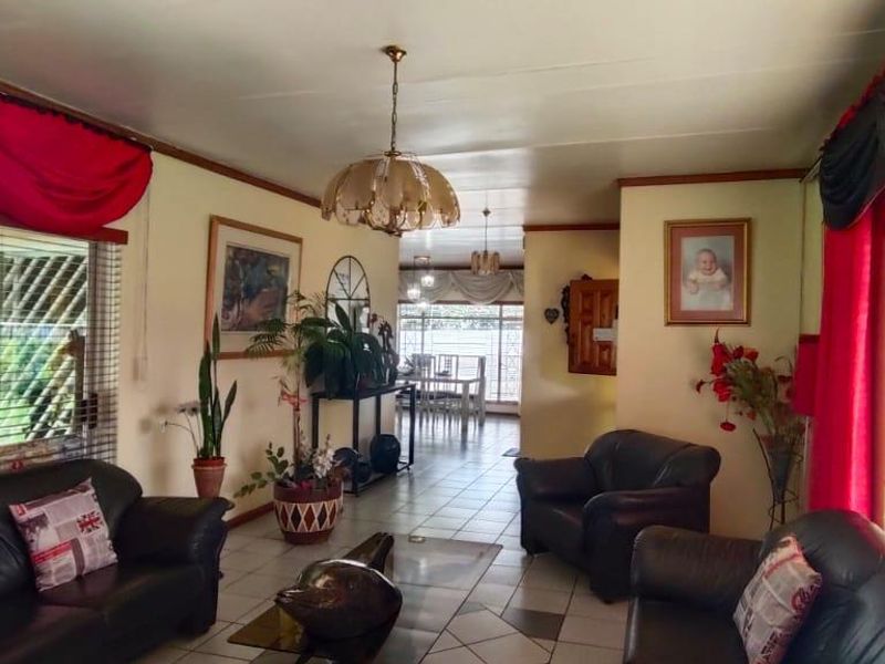 Spacious living room featuring tiled flooring, large windows with venetian blinds, and a central ceiling light fixture, offering a bright and open layout.