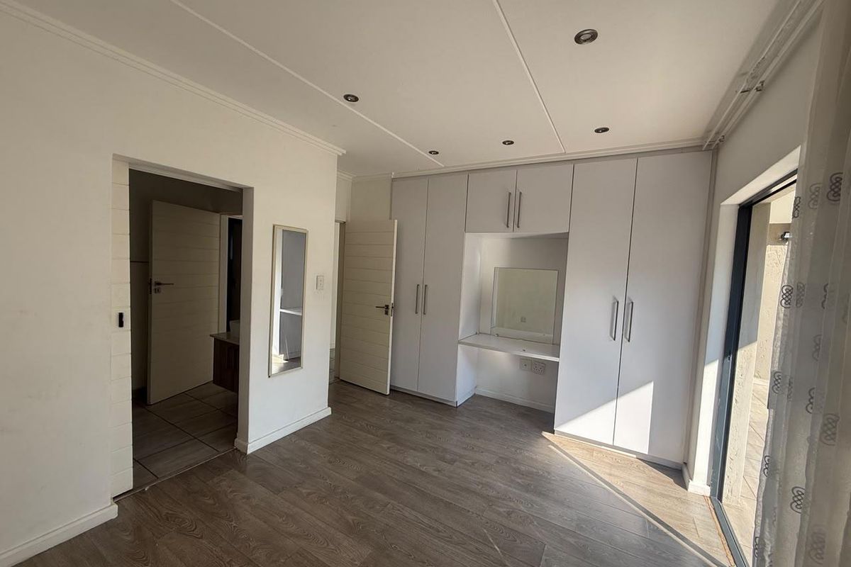 A bright, empty bedroom featuring modern laminate flooring, extensive built-in cupboards with an integrated vanity nook, and direct access to an outdoor area.